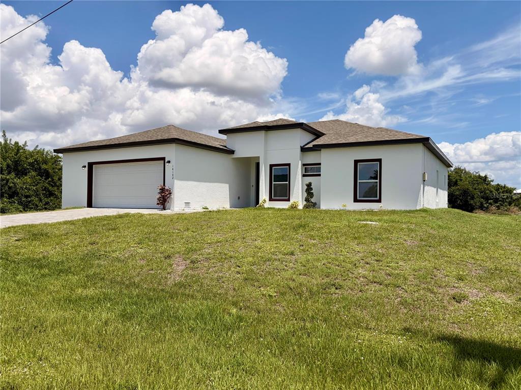 A white, single-story house with a two-car garage sits on a grassy, sloped lot — 14142 APPLETON BOULEVARD, PORT CHARLOTTE, FL