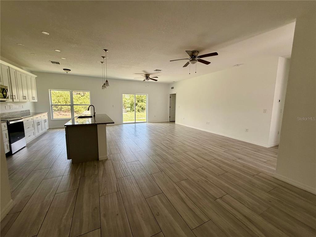 An open-concept kitchen and living area featuring white cabinets, a kitchen island, and wood-look flooring — 14142 APPLETON BOULEVARD, PORT CHARLOTTE, FL