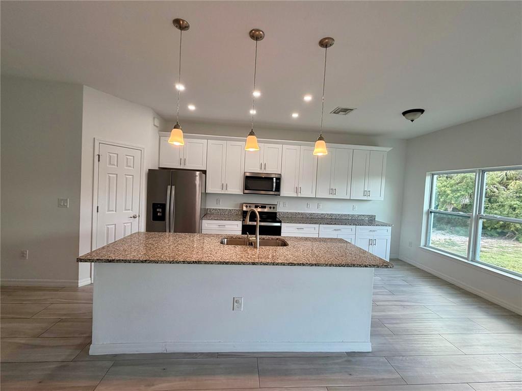 A kitchen features a granite-topped island, white cabinetry, stainless steel appliances, and tile flooring — 14142 APPLETON BOULEVARD, PORT CHARLOTTE, FL