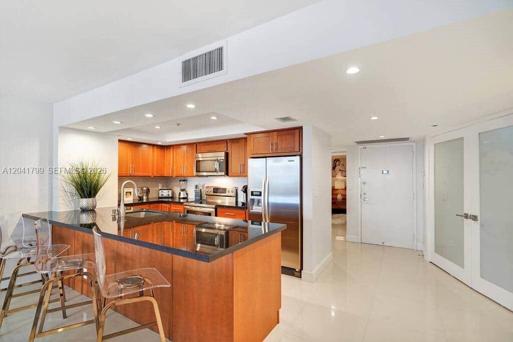 A kitchen features wood cabinets, black countertops, stainless steel appliances, and a breakfast bar — 1717 N Bayshore Dr # 2056, Miami FL 33132, MIAMI, FL