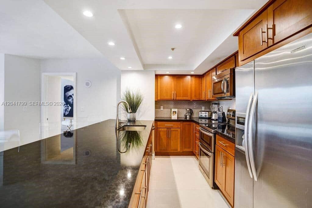 A kitchen features wood cabinets, stainless steel appliances, and a long black granite countertop — 1717 N Bayshore Dr # 2056, Miami FL 33132, MIAMI, FL