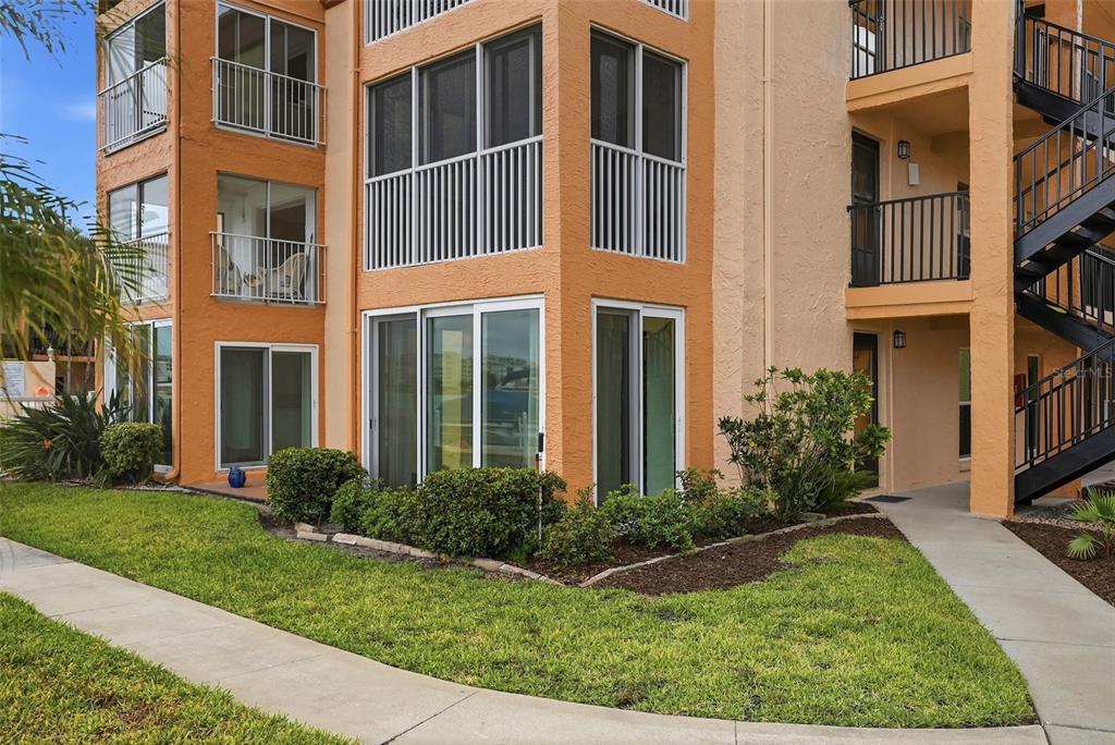 An exterior view of a multi-story orange apartment building with balconies and a concrete walkway — 8921 BLIND PASS ROAD UNIT 144, ST PETE BEACH, FL