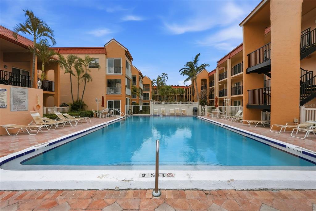 A rectangular swimming pool is centered between two multi-story apartment buildings with balconies — 8921 BLIND PASS ROAD UNIT 144, ST PETE BEACH, FL