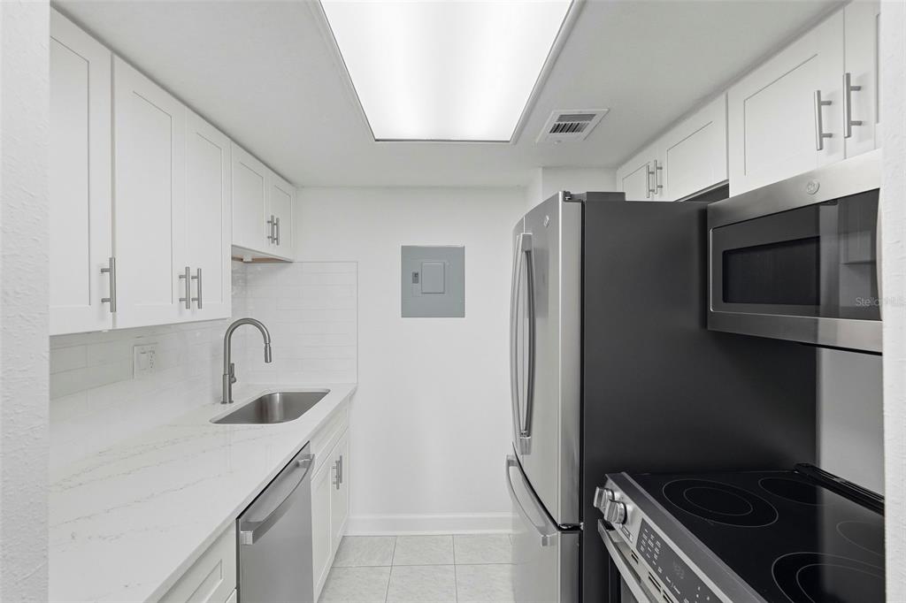 A galley kitchen features white cabinets, stainless steel appliances, and light-colored countertops — 8921 BLIND PASS ROAD UNIT 144, ST PETE BEACH, FL