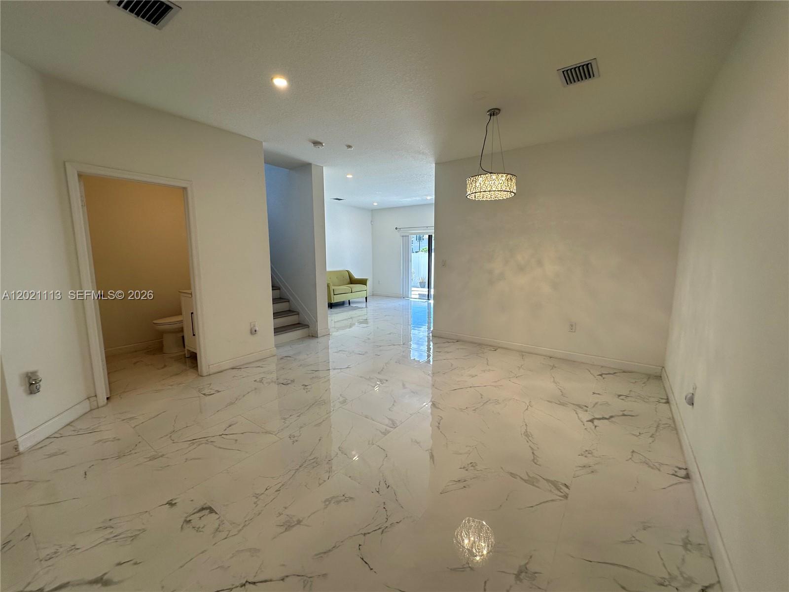 An open-concept room features white marble-look tile flooring, a modern chandelier, and a staircase — 20352 NW 6th Ave, Miami Gardens FL 33169, MIAMI GARDENS, FL
