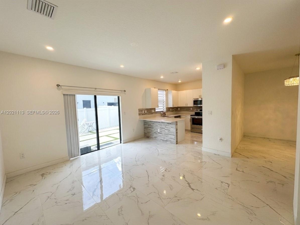 An open-concept kitchen and living area feature white marble-look tile flooring and sliding glass doors — 20352 NW 6th Ave, Miami Gardens FL 33169, MIAMI GARDENS, FL