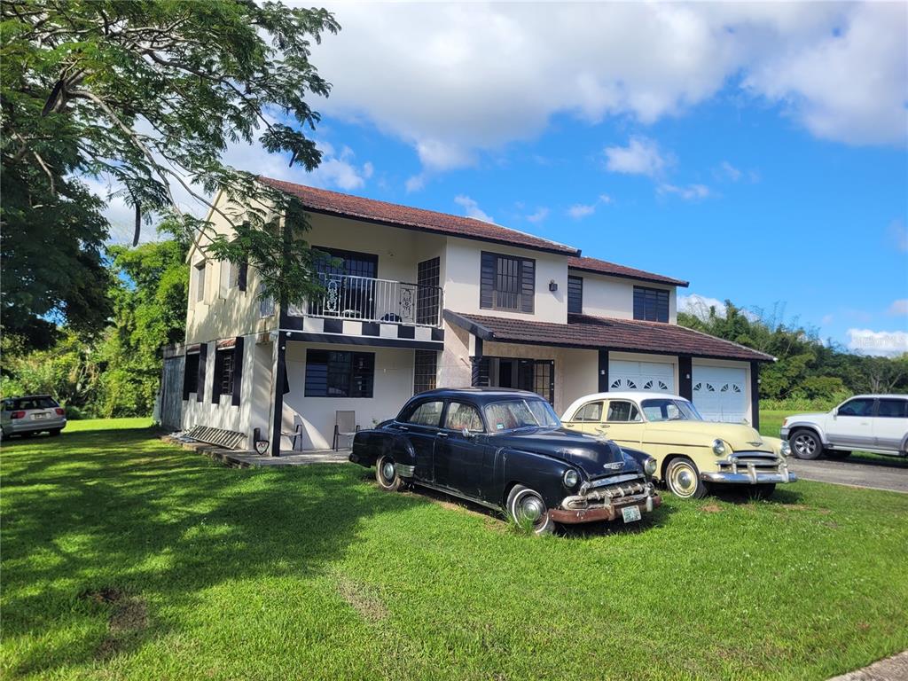 A two-story house with a balcony and two vintage cars parked on the front lawn — 743 PR 743, CAYEY, PR