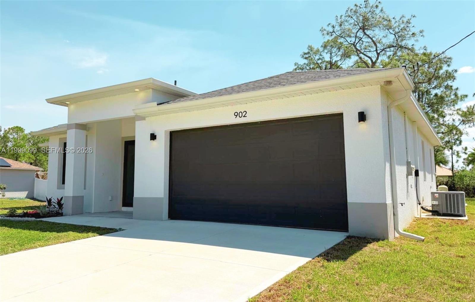 A single-story house features a white exterior, a dark garage door, and a concrete driveway — 902 MAGNOLIA AVE, Lehigh Acres FL 33972, LEHIGH ACRES, FL