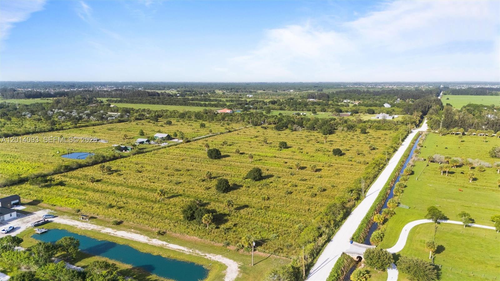 An aerial view shows a large, grassy lot with a canal and scattered trees — 21st SW & 58th Ave, Vero Beach FL 32968, VERO BEACH, FL
