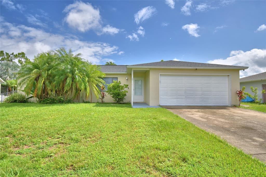 A single-story house with a white garage door, a front entrance, and a palm tree — 2123 RAMSDALE DRIVE SE, PALM BAY, FL