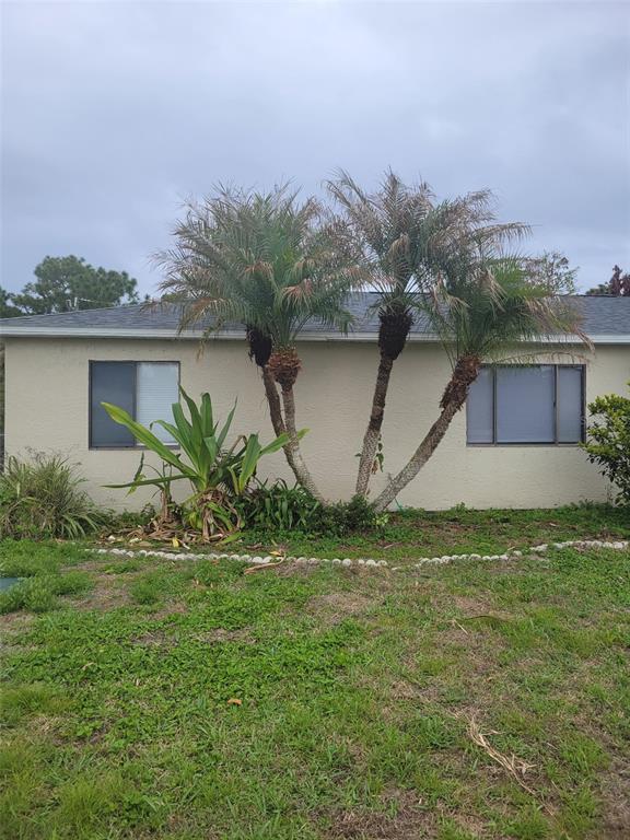 A beige house exterior features three palm trees and a large plant in the yard — 2123 RAMSDALE DRIVE SE, PALM BAY, FL