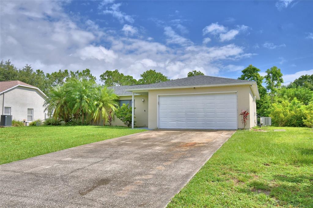 A single-story house with a white garage door and a concrete driveway under a blue sky — 2123 RAMSDALE DRIVE SE, PALM BAY, FL