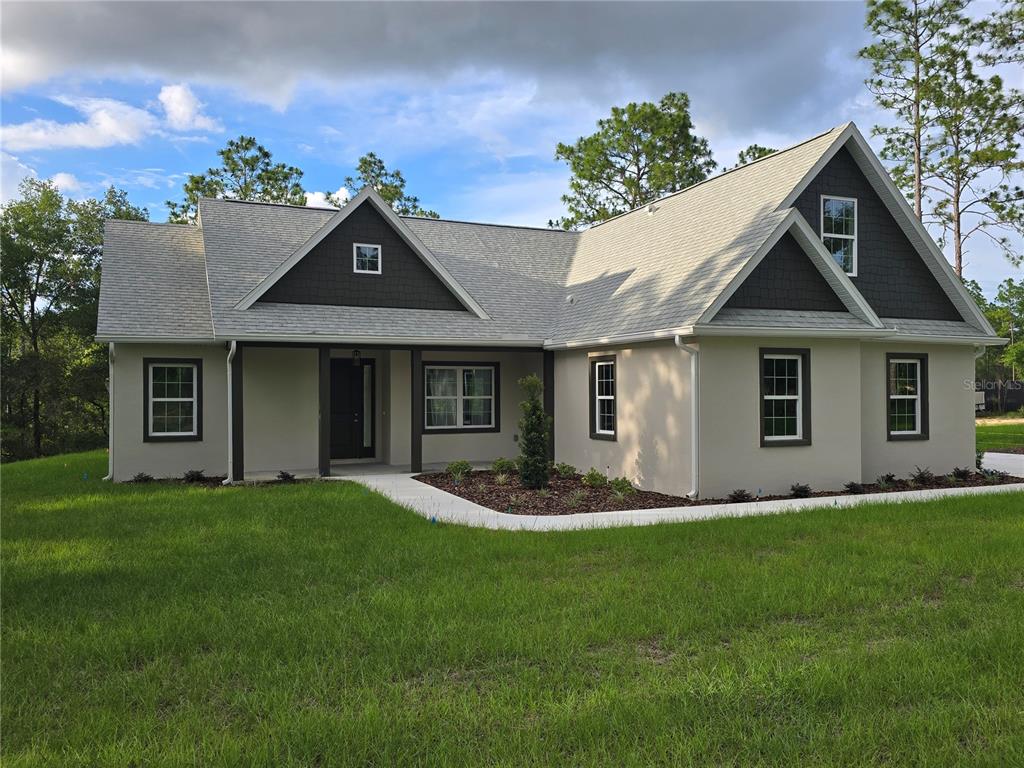 A single-story house with a light-colored stucco exterior, dark shingle gables, and a front porch — 13193 BARNEVELDE ROAD, WEEKI WACHEE, FL
