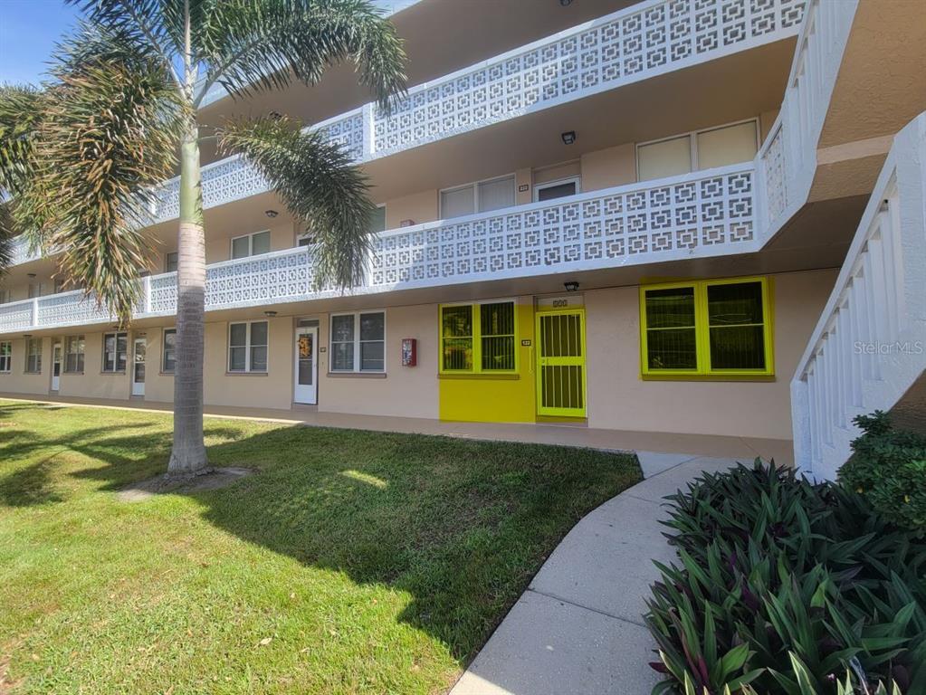 A three-story apartment building exterior features a concrete walkway, palm tree, and yellow-framed windows — 4915 BAY STREET NE UNIT 122, ST PETERSBURG, FL