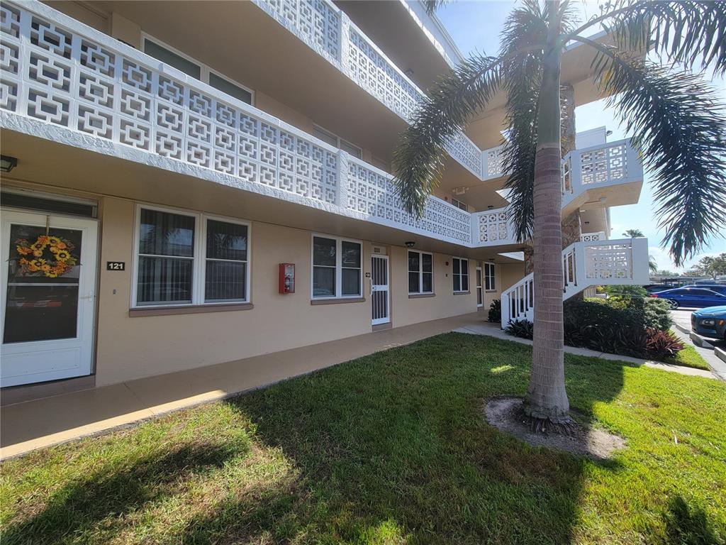 A multi-story apartment building exterior features a palm tree, a lawn, and white railings — 4915 BAY STREET NE UNIT 122, ST PETERSBURG, FL