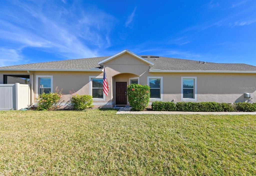 A single-story house with a tan stucco exterior, a dark front door, and a front lawn — 13529 CREST LAKE DRIVE, HUDSON, FL