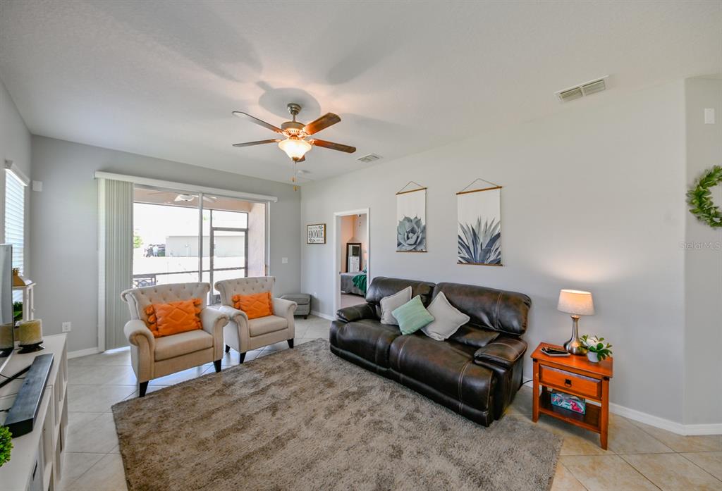 A living room features a dark leather sofa, two beige armchairs, and a ceiling fan — 13529 CREST LAKE DRIVE, HUDSON, FL