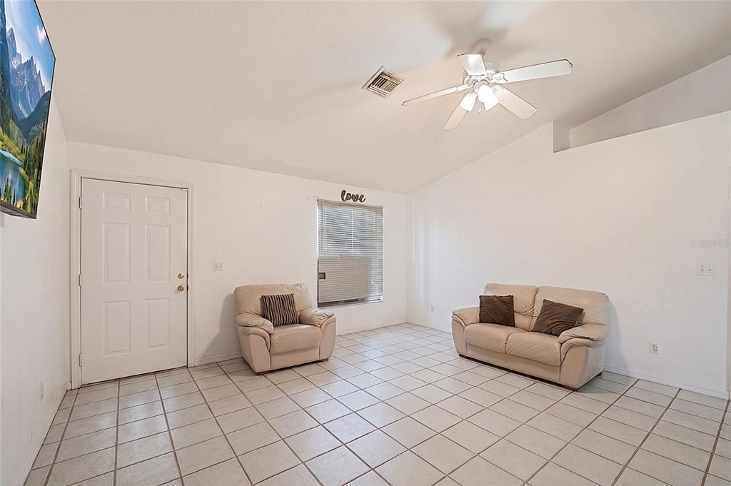 A living room with white walls, tiled floors, a ceiling fan, and two beige sofas — 2331 JAYLEN WATKINS STREET, FORT MYERS, FL