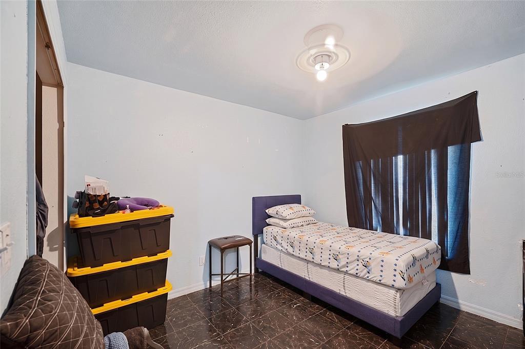 A bedroom with light blue walls, dark tile flooring, a single bed, and storage bins — 2331 JAYLEN WATKINS STREET, FORT MYERS, FL