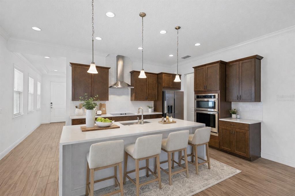 A modern kitchen features dark wood cabinetry, a large white island with seating, and stainless appliances — 13300 BROMBOROUGH DRIVE, ORLANDO, FL