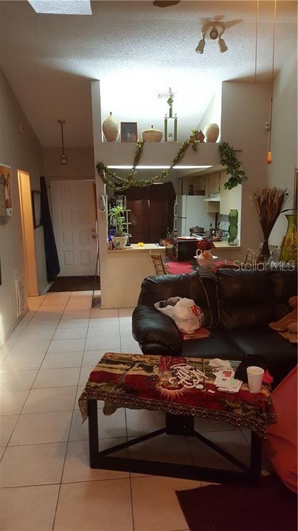 A living room with tile floors, a black leather sofa, and a kitchen pass-through window — 2806 SHINING WILLOW TERRACE, ORLANDO, FL