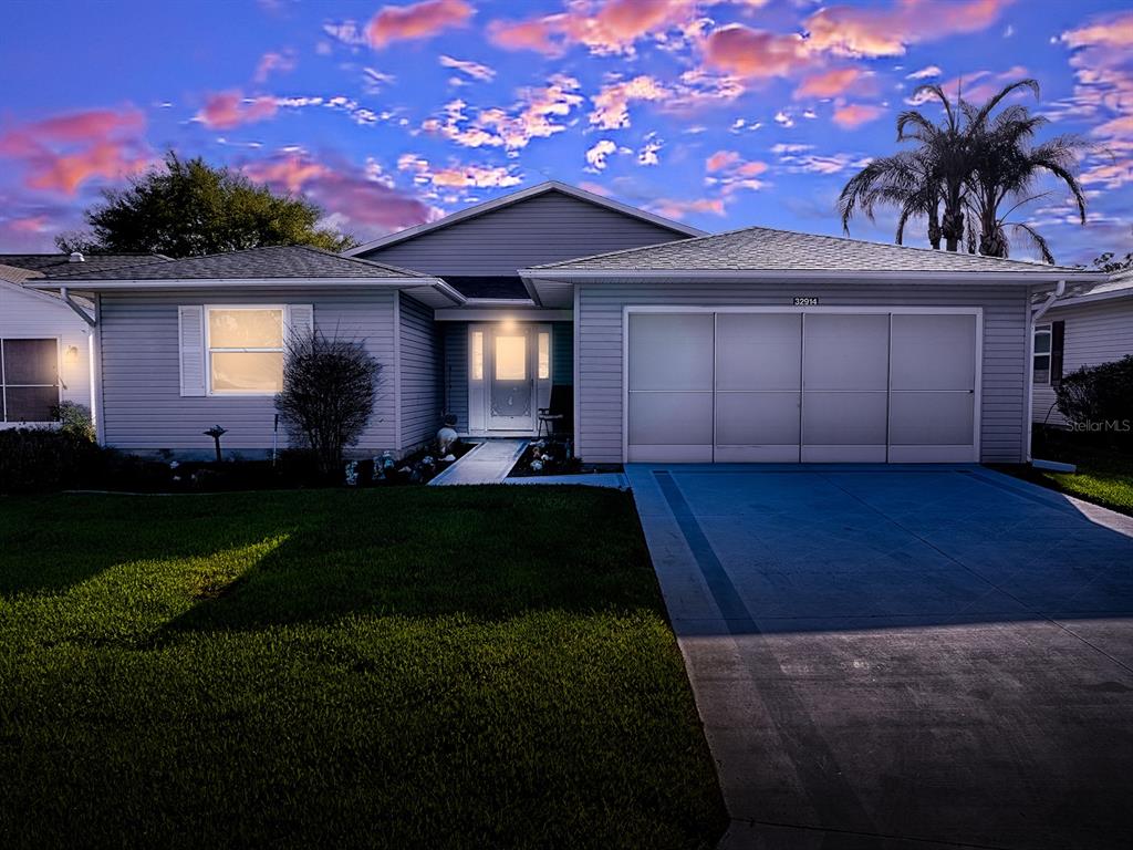 A single-story house with light gray siding, a three-car garage, and a concrete driveway — 32914 CROOKED OAKS LANE, LEESBURG, FL