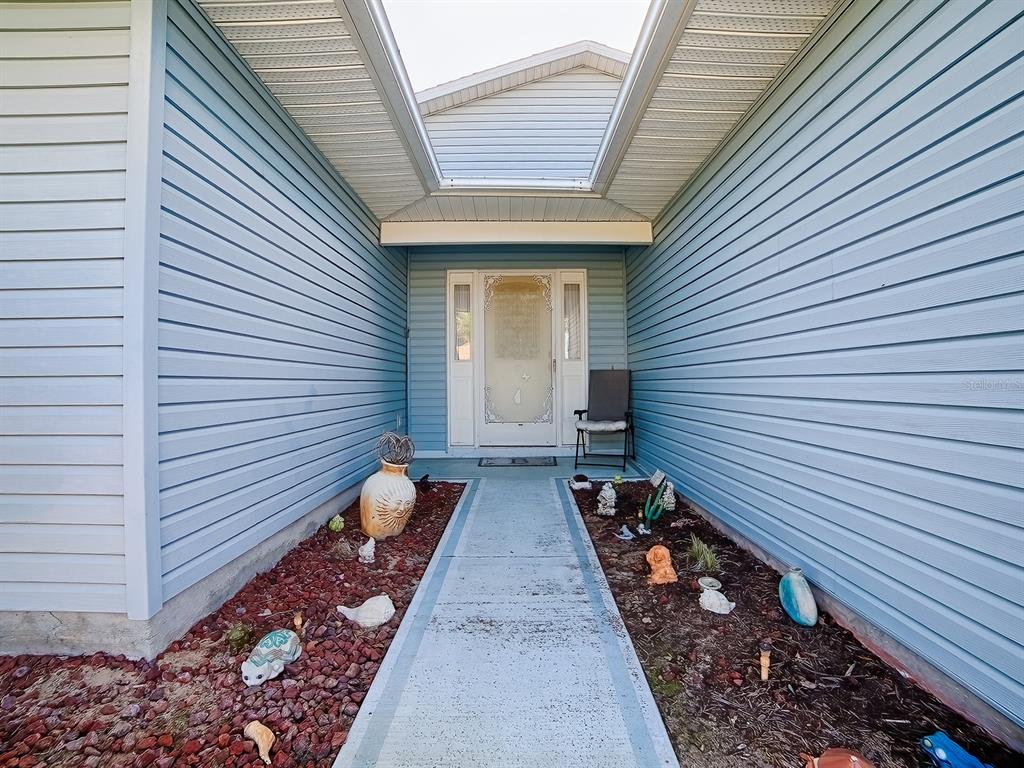 A concrete walkway leads to the front door of a house with light blue siding — 32914 CROOKED OAKS LANE, LEESBURG, FL