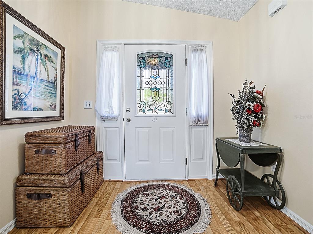 An entryway features a stained-glass front door, wicker storage trunks, and a decorative cart — 32914 CROOKED OAKS LANE, LEESBURG, FL