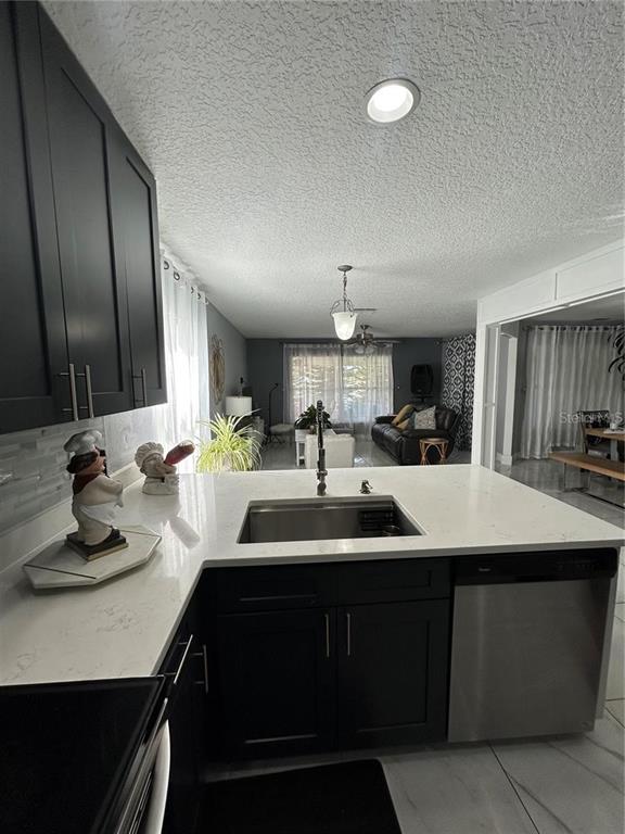 A kitchen island with a stainless steel sink and white countertop overlooks a living room — 1906 SHERBOURNE STREET, WINTER GARDEN, FL