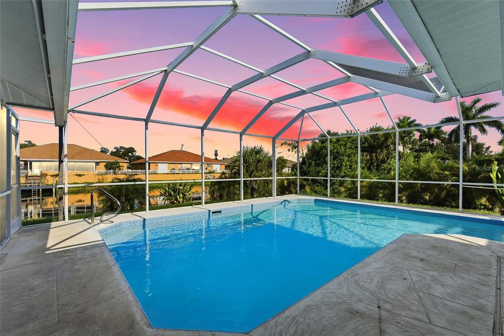 A screened-in swimming pool patio overlooks a canal and neighboring houses at sunset — 524 SE 8TH PLACE, CAPE CORAL, FL