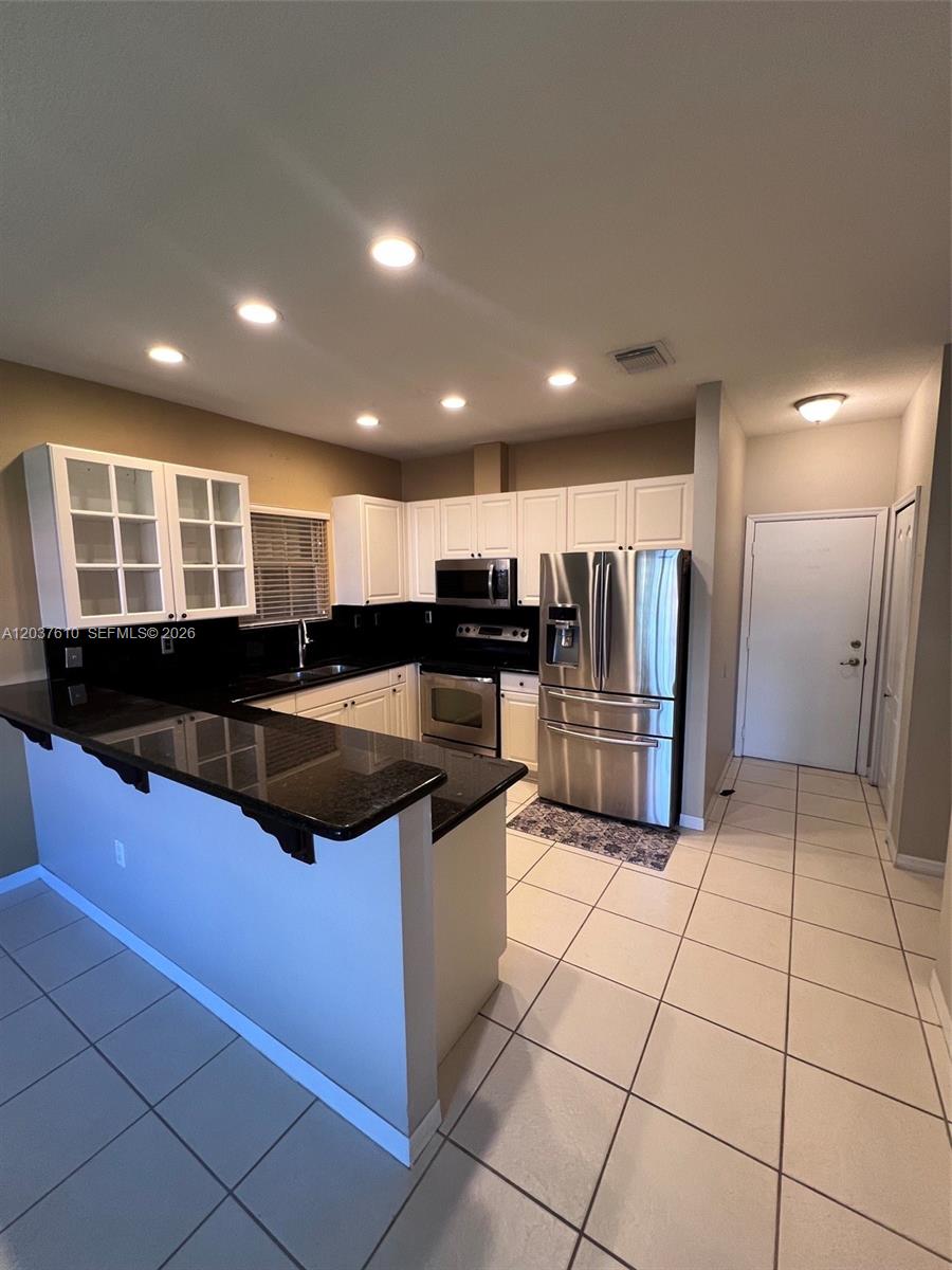 A kitchen features white cabinets, black countertops, stainless steel appliances, and light-colored tile flooring — 10155 SW 159th Ct, Miami FL 33196, MIAMI, FL