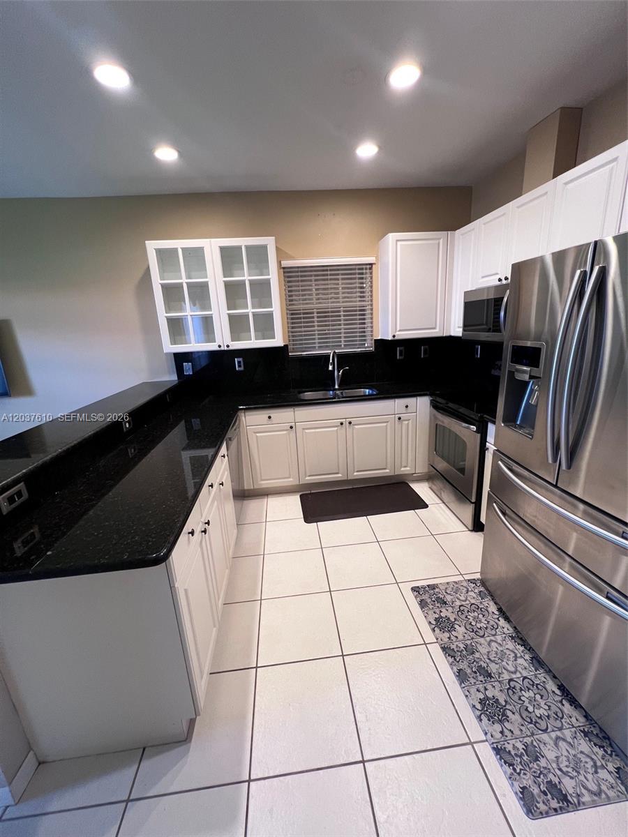 A kitchen features white cabinets, black countertops, stainless steel appliances, and white tiled flooring — 10155 SW 159th Ct, Miami FL 33196, MIAMI, FL