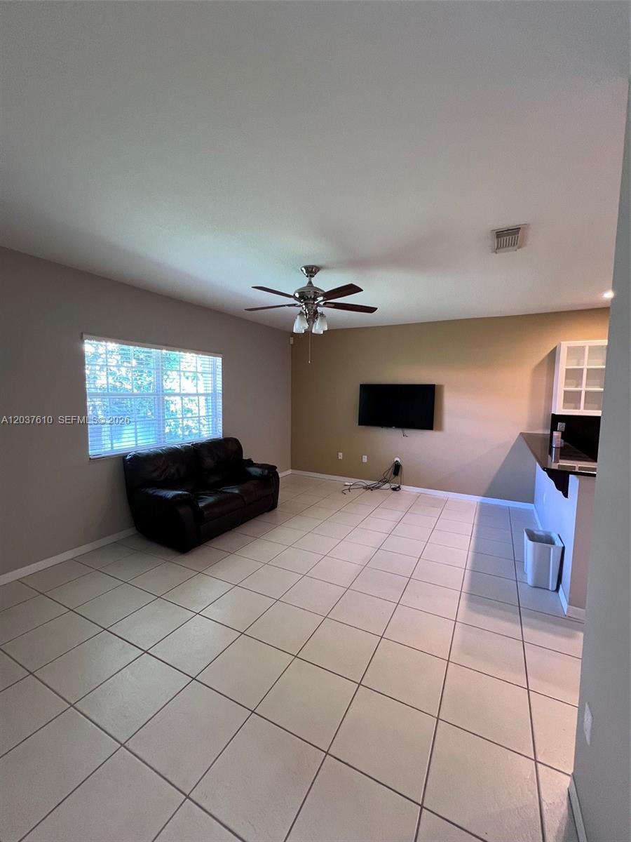 A living room features light-colored tile flooring, a black leather sofa, and a wall-mounted television — 10155 SW 159th Ct, Miami FL 33196, MIAMI, FL