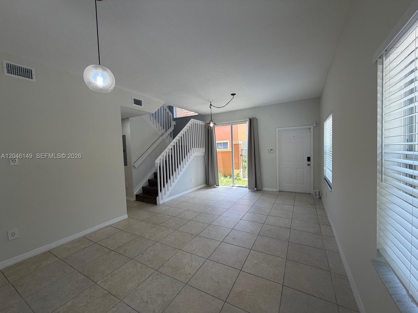 An open living area features tile flooring, a staircase with white railings, and sliding glass doors — 2201 Clipper Pl # 5405, Dania Beach FL 33312, DANIA BEACH, FL