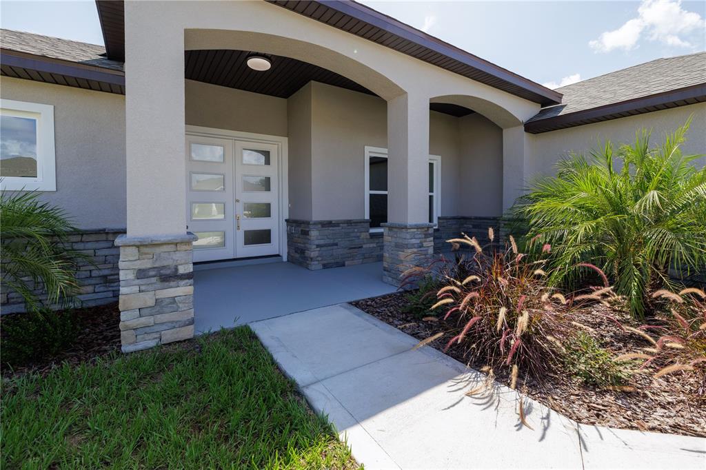 A concrete walkway leads to the covered entryway of a house with stone veneer accents — 23 FRANCIS LANE, PALM COAST, FL