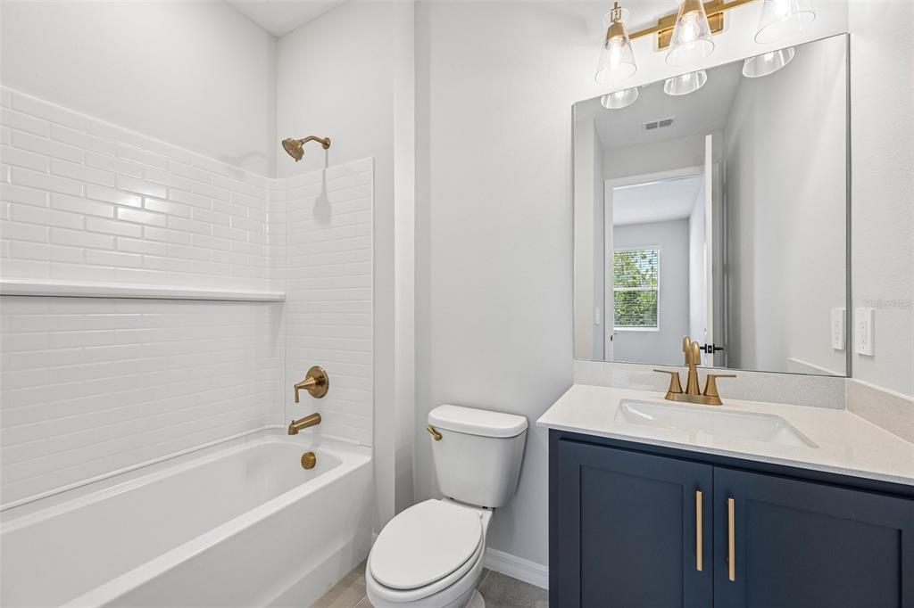 A bathroom features a white subway-tiled tub, a toilet, and a navy vanity with gold hardware — 9927 HIDDEN HAMMOCK LOOP, PARRISH, FL