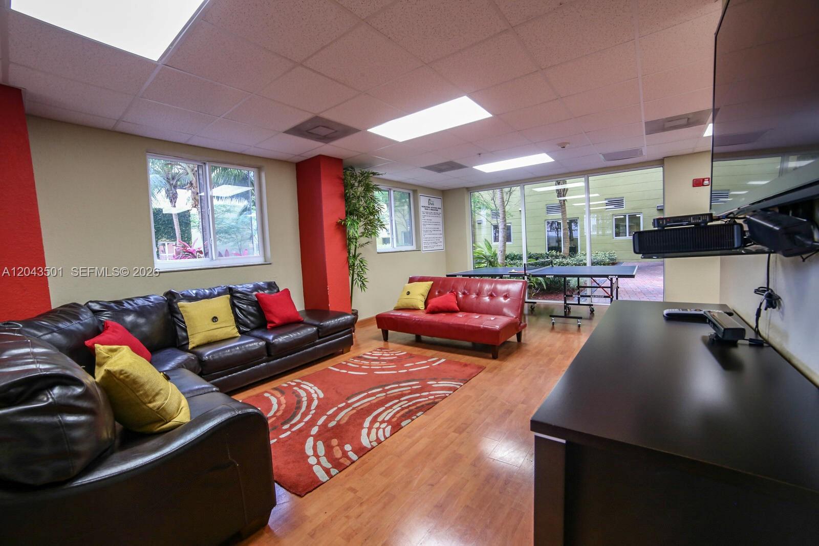 A lounge area features a leather sectional, a red sofa, a ping pong table, and windows — 7901 NW 7th Ave # 1102, Miami FL 33150, MIAMI, FL
