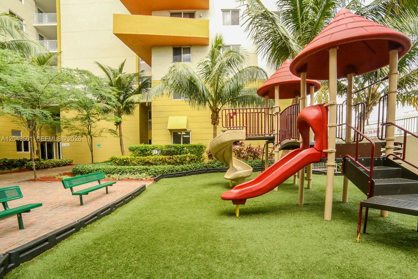 A playground with a slide and climbing structure sits on a lawn near a building — 7901 NW 7th Ave # 1102, Miami FL 33150, MIAMI, FL