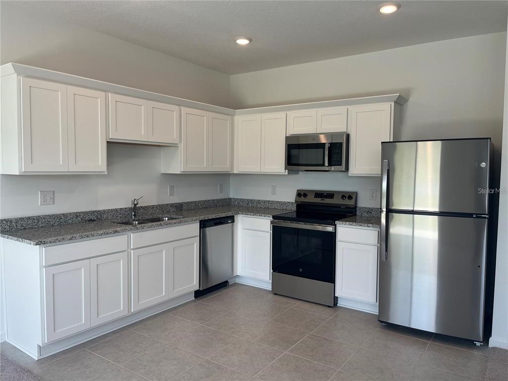 A kitchen features white cabinets, granite countertops, stainless steel appliances, and tile flooring — 3301 VESARA DRIVE, DAVENPORT, FL