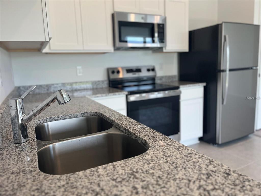 A kitchen features white cabinets, granite countertops, a stainless steel sink, and stainless steel appliances — 3301 VESARA DRIVE, DAVENPORT, FL