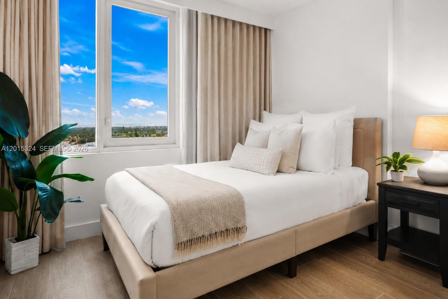 A bedroom features a beige upholstered bed, a window with a view, and a nightstand — 2301 Collins Ave # 1128, Miami Beach FL 33139, MIAMI BEACH, FL