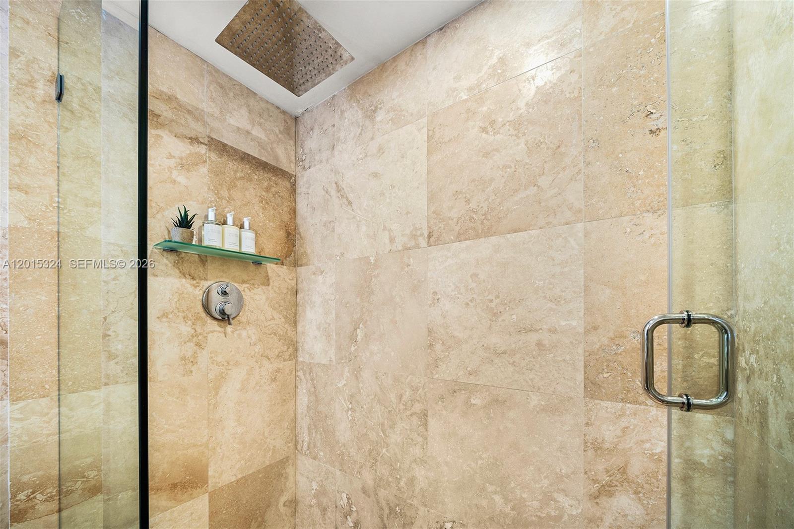 A walk-in shower features beige stone tile walls, a glass shelf, and a rainfall showerhead — 2301 Collins Ave # 1128, Miami Beach FL 33139, MIAMI BEACH, FL