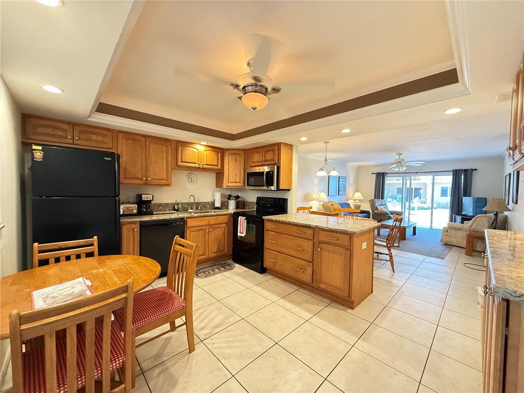 A kitchen with wood cabinets and granite countertops opens into a living area with tile — 111 N ATLANTIC AVENUE UNIT A105, NEW SMYRNA BEACH, FL