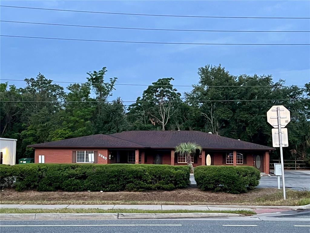 A single-story red brick building with a dark shingled roof sits behind a manicured hedge — 3360 US HIGHWAY 441/27, FRUITLAND PARK, FL