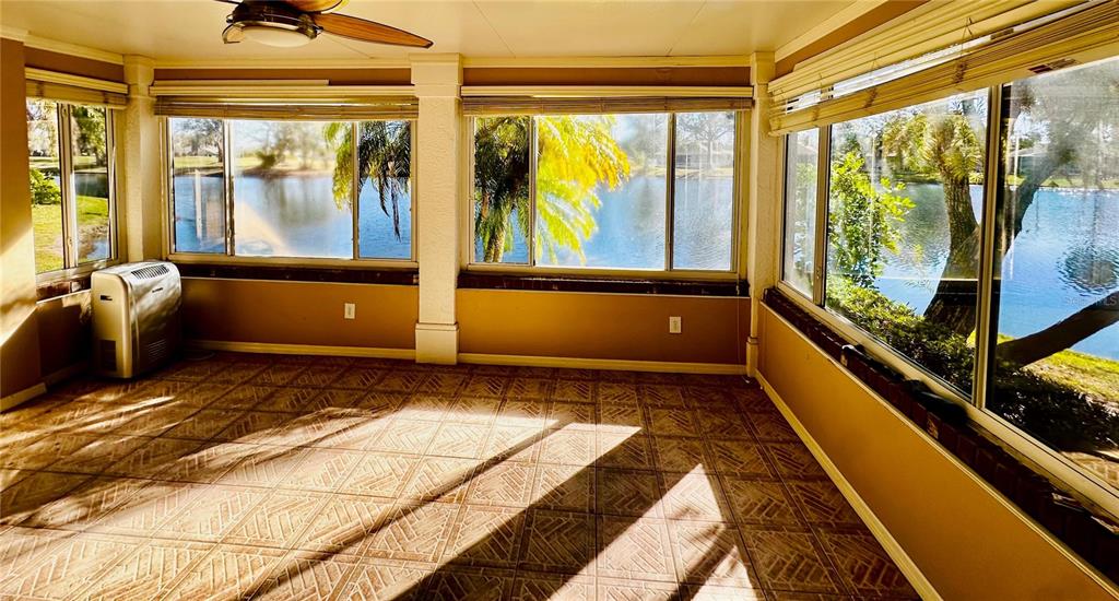 A sunroom with tiled floors, large windows overlooking a lake, and a portable air conditioner — 801 SILVERTHORN LANE, SUN CITY CENTER, FL