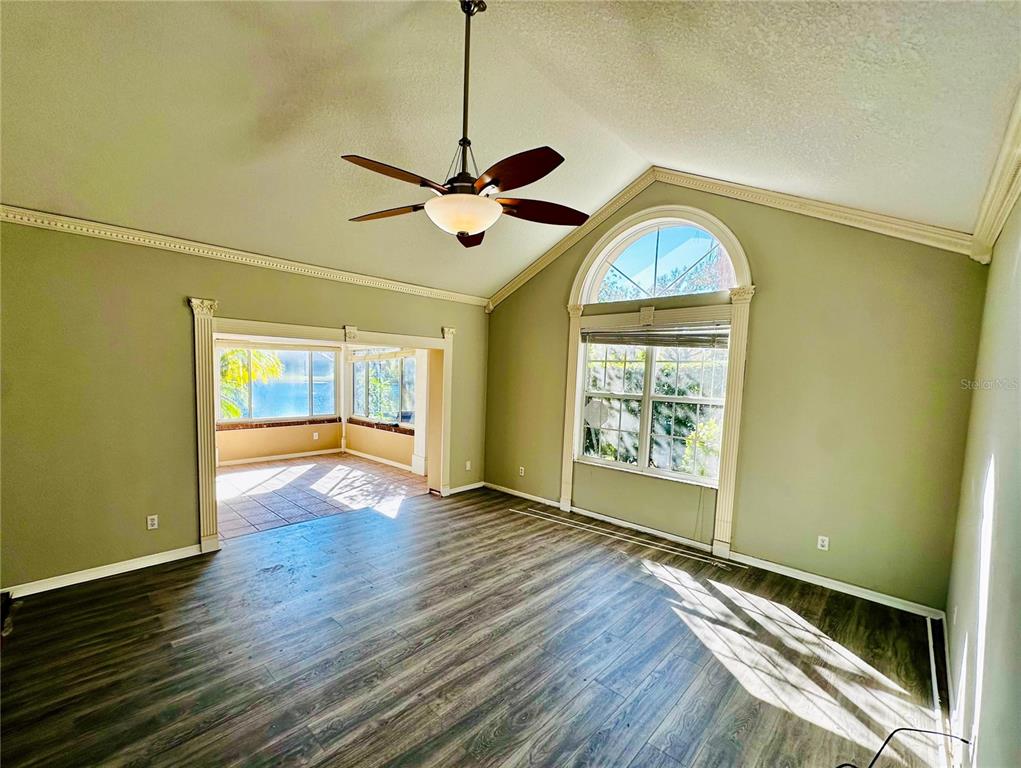 A living room with wood-look flooring, a vaulted ceiling, a ceiling fan, and arched windows — 801 SILVERTHORN LANE, SUN CITY CENTER, FL