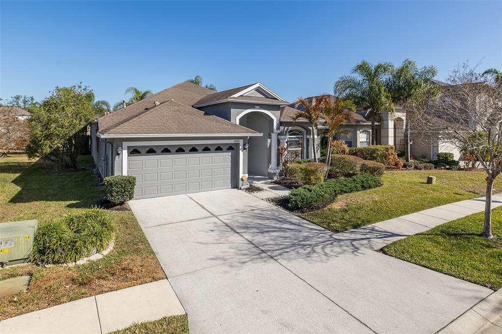A single-story suburban house with a gray garage, arched entryway, and a concrete driveway — 20301 FALLING ROCK DRIVE, LAND O LAKES, FL