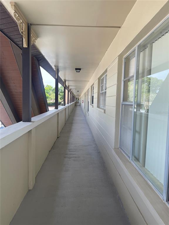 An outdoor apartment building walkway with a concrete floor, beige walls, and large windows — 2295 BELGIAN LANE UNIT 43, CLEARWATER, FL