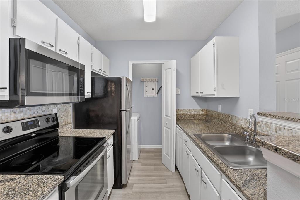 A galley-style kitchen features white cabinets, granite countertops, stainless steel appliances, and a tiled backsplash — 4320 S KIRKMAN ROAD UNIT 1511, ORLANDO, FL