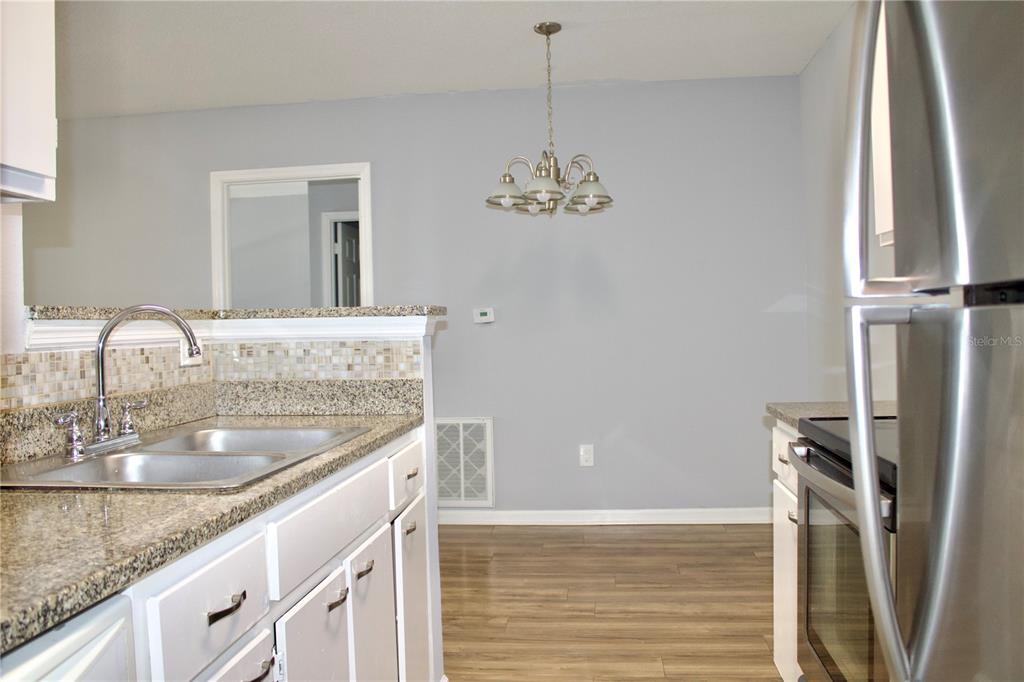 A kitchen with white cabinets, granite countertops, a stainless steel sink, and a dining area — 4320 S KIRKMAN ROAD UNIT 1511, ORLANDO, FL